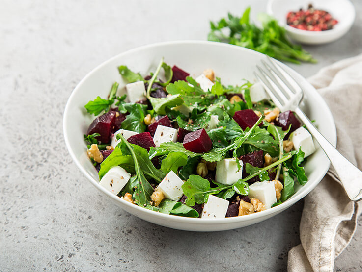 Beetroot and rocket salad with feta cheese and walnuts served in a white bowl.