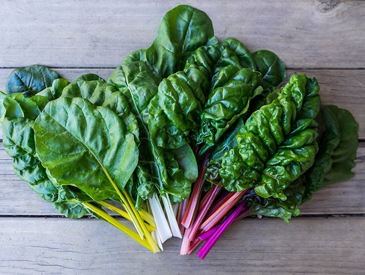 A bouquet of silverbeet or rainbow chard as it's also known fanned out against a wooden surface. The silverbeet has yellow, white and purple stalks.