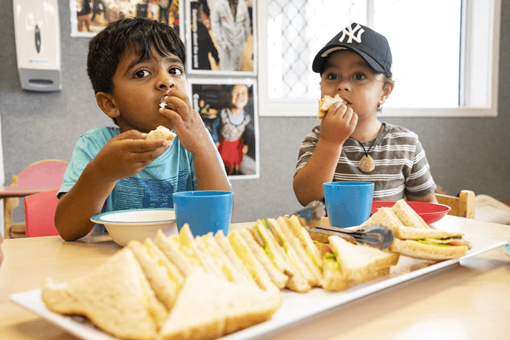 Two small boys enjoying a shred lunch of sandwiches at their early learning centre.
