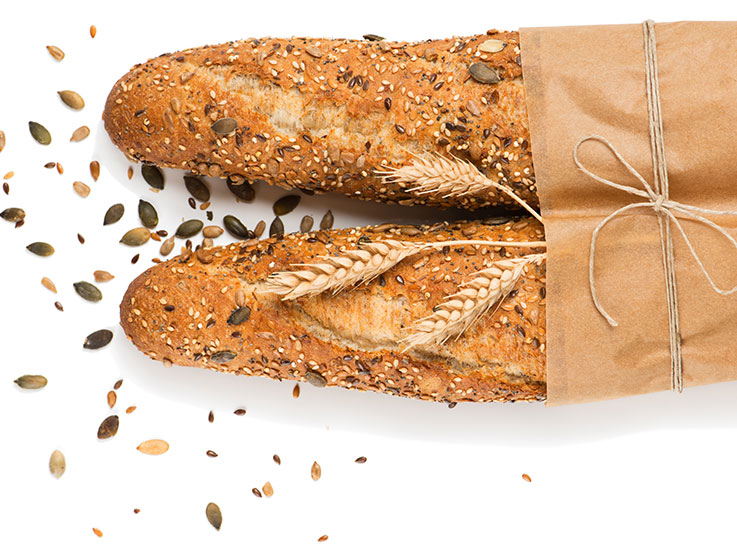 Top view of two baguettes baked bread in paper with different seeds (pumpkin, poppy, flax, sunflower, sesame, millet) decorated with ears of wheat isolated on white background.