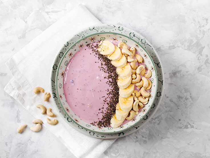 Healthy breakfast berry smoothie bowl topped with banana, cashew and chia seeds