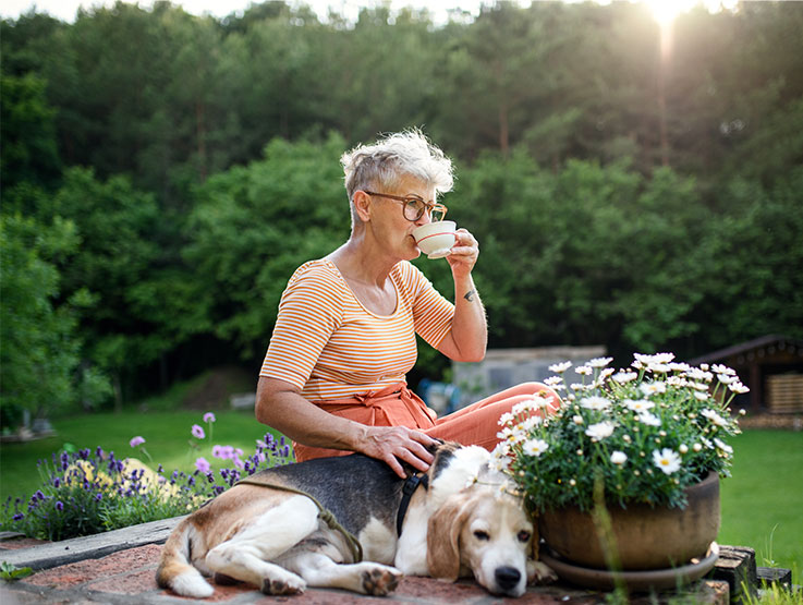 Senior woman drinking tea in her garden with her dog