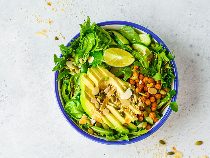 Green healthy salad with avocado, baked chickpeas and seeds in a white bowl.